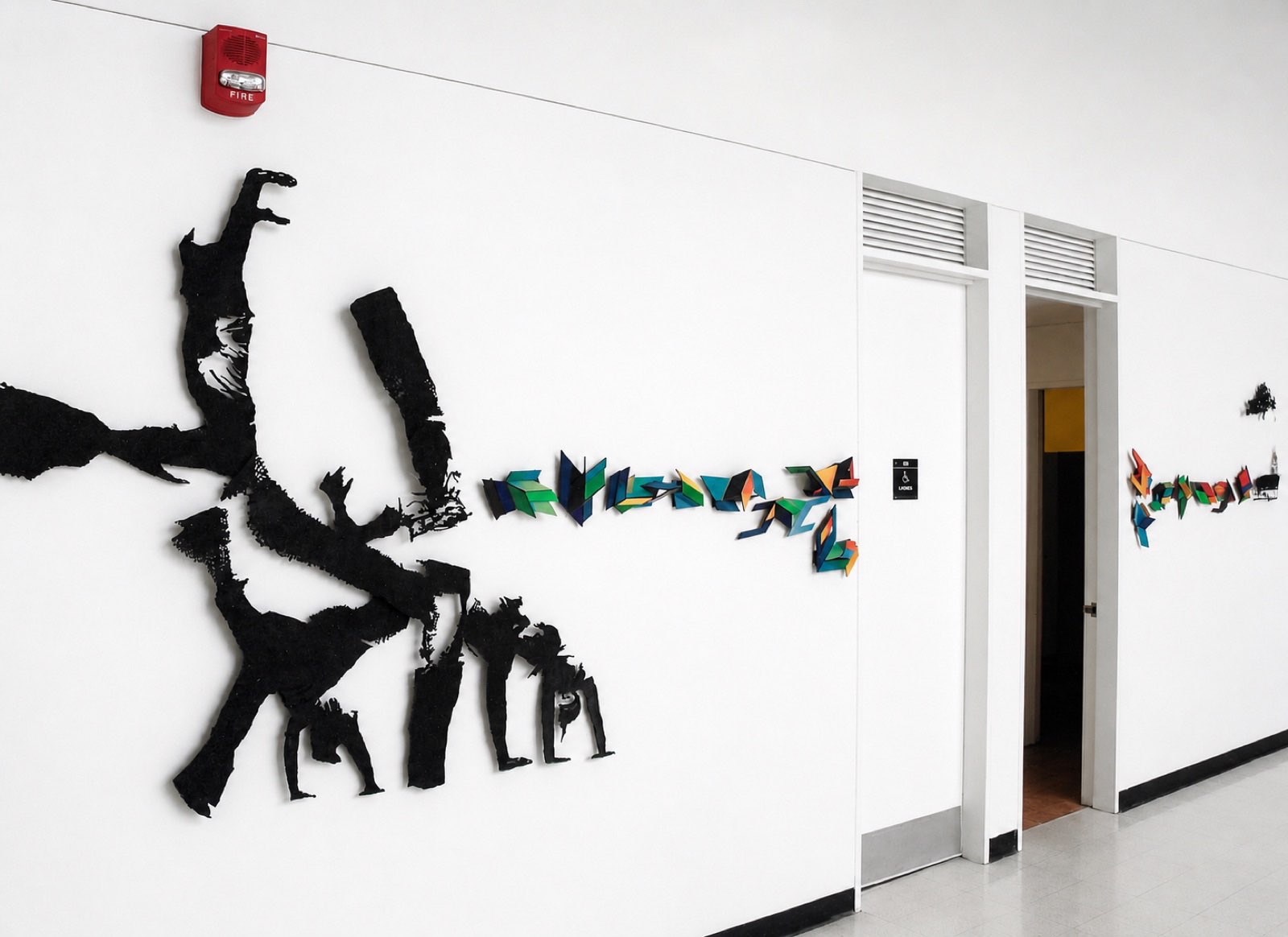 Corridor installation — black cut-out figures dissolving into folded color fragments along a hallway